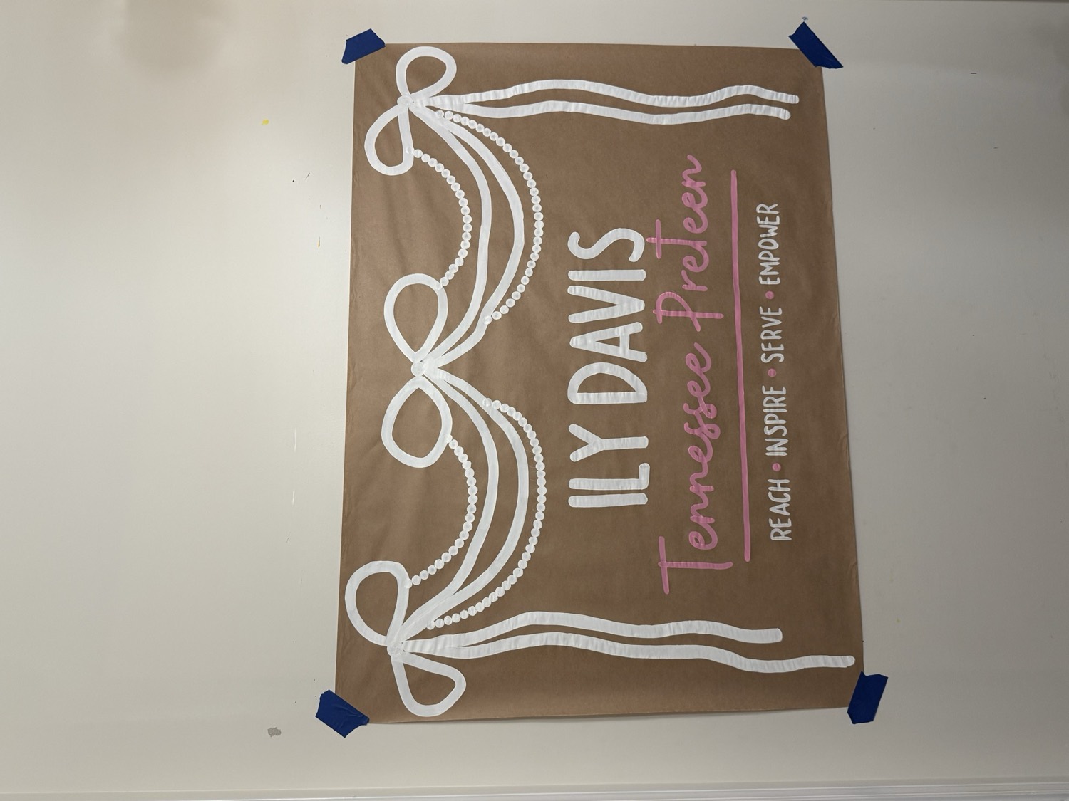 Brown paper banner reading Ily Davis, Tennessee Preteen, Reach Inspire Serve Empower, under painted white ribbon bows and strings of pearls.