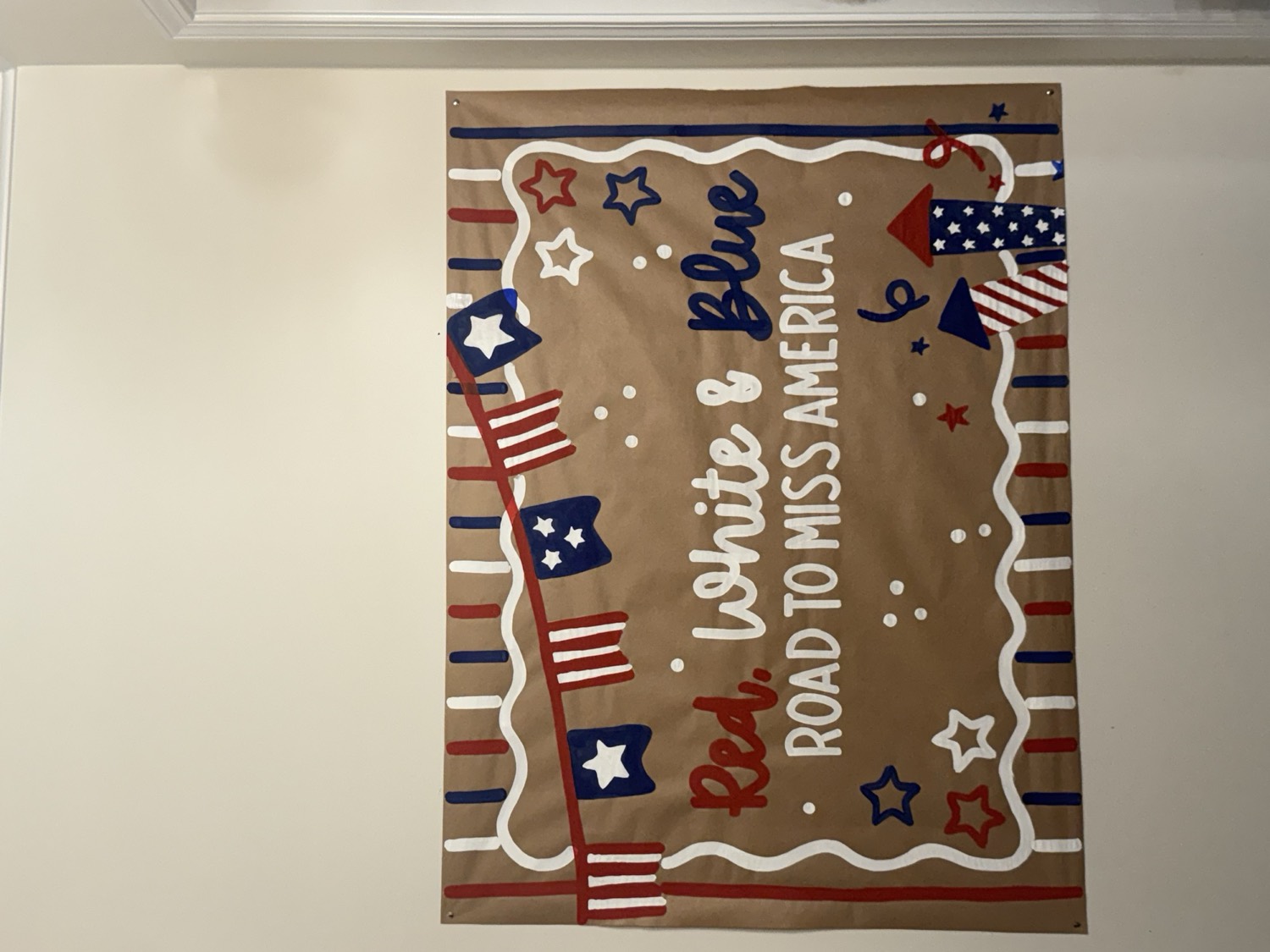 Brown paper banner reading Red, White and Blue, Road to Miss America, with painted bunting, stars and two firework rockets.